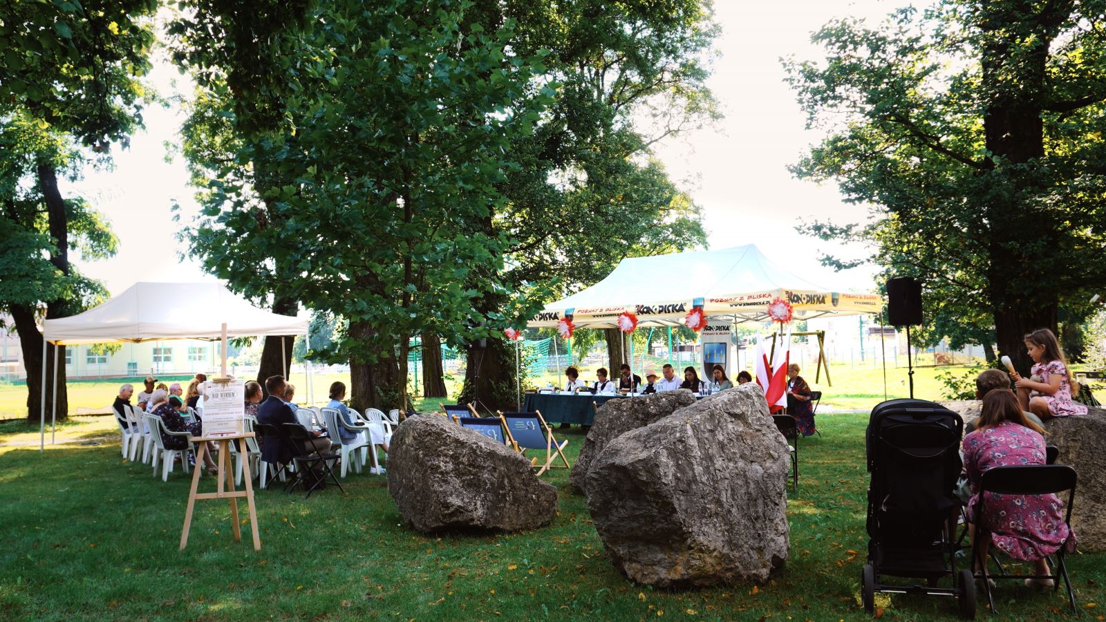 Zdjęcie przedstawia namiot z osobami czytającymi oraz publiczność siedzącą przed występującymi. 